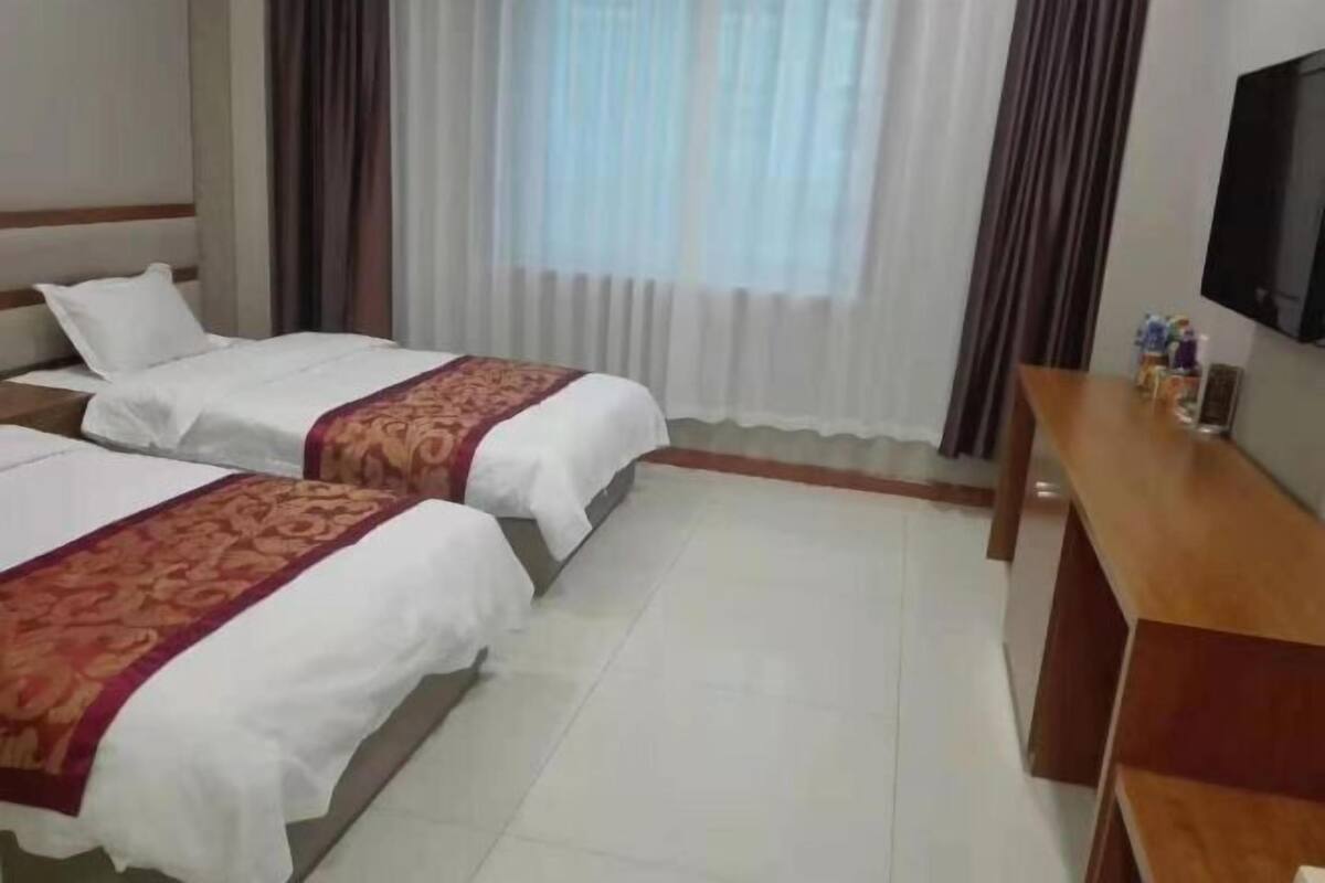 Una habitación de hotel con dos camas, un escritorio de madera, un televisor de pantalla plana y una ventana con cortinas.