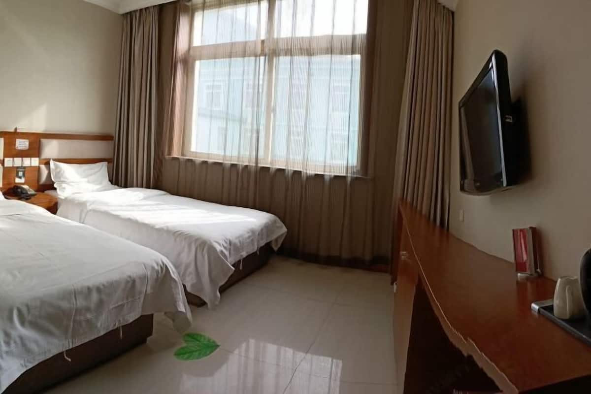 Habitación de hotel con dos camas, un televisor montado en la pared y una ventana con cortinas.