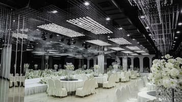 A banquet hall with round tables, white floral centerpieces, and a ceiling adorned with hanging lights.