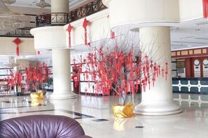 Un vestíbulo con grandes columnas blancas, un piso con diseño de cuadros y adornos rojos colgando del techo.