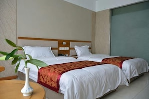 A hotel room with two beds, a bedside table, a vase with a plant, and a large window.