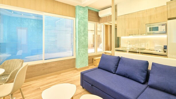 A modern hotel room with a blue sofa, wooden flooring, a glass partition, and a kitchenette. - GuestReady - Bright and Cozy studio in Salamanca (Salamanca)