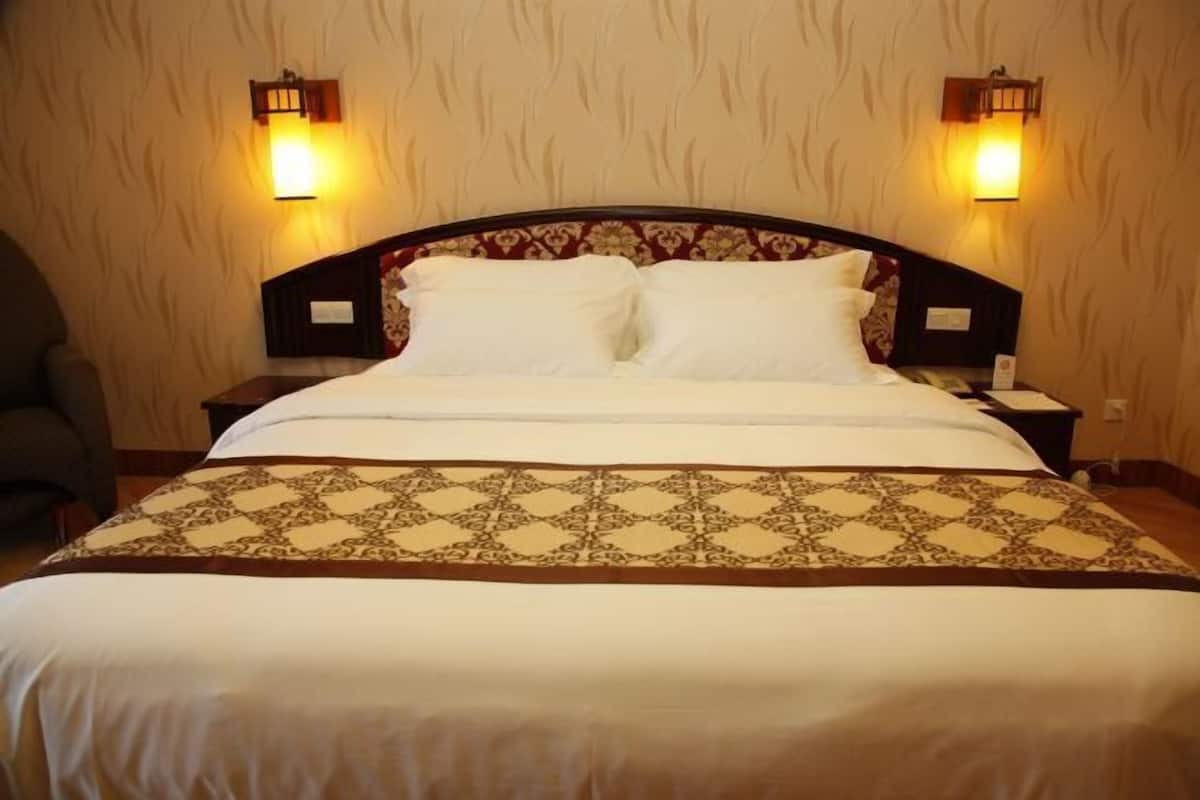 A hotel room with a large bed, two bedside lamps, and a patterned bedspread.