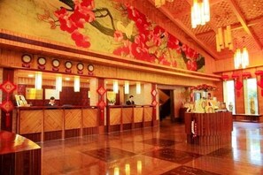 A hotel lobby with a reception desk, a large floral mural on the wall, and a polished floor. - Yannanfei Weilong Hotel (Meizhou)