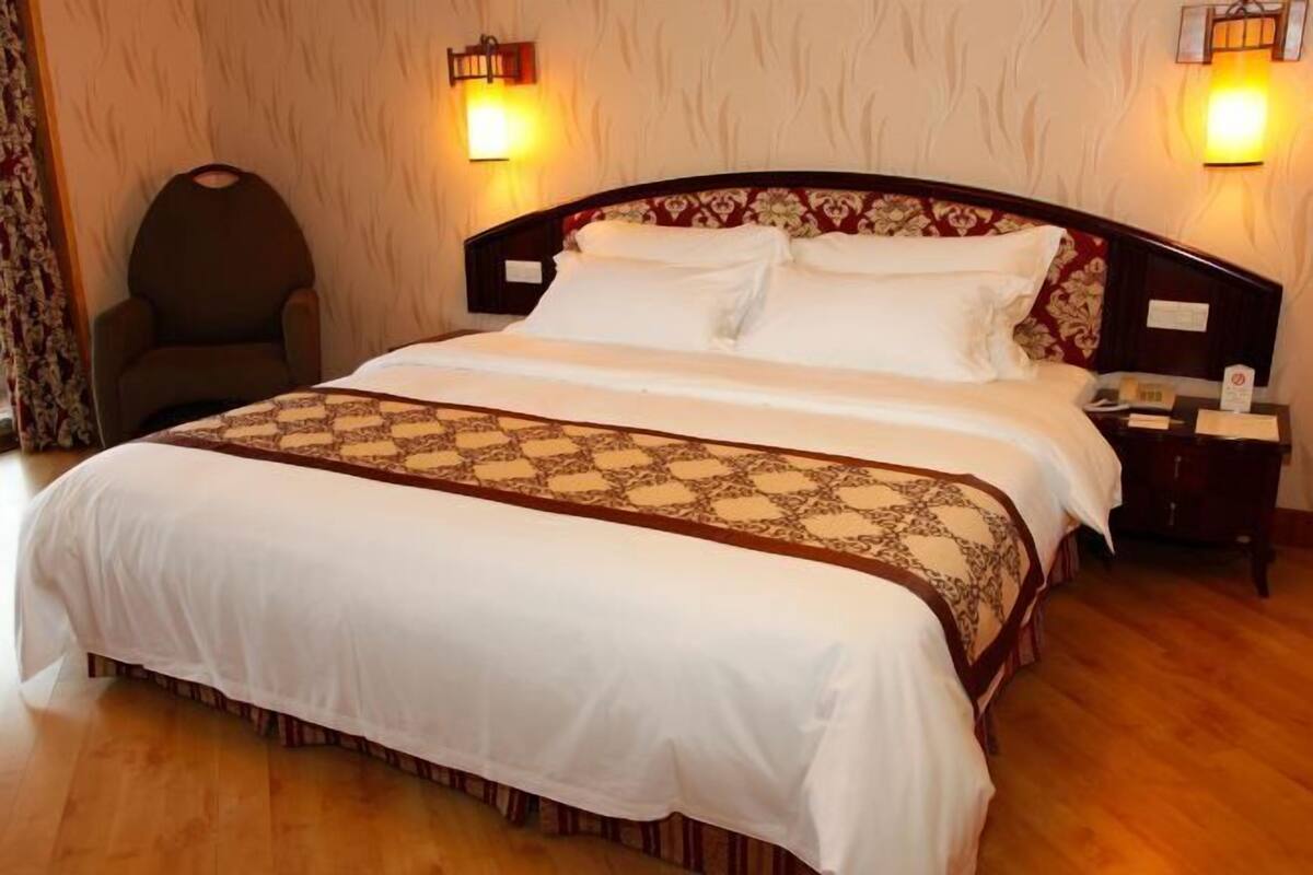 A neatly made bed with a patterned bedspread, a wooden headboard, and two wall-mounted lamps.