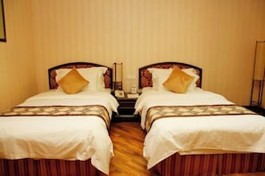 A hotel room with two single beds, each with a patterned bedspread and pillows, a wooden floor, and a mirror between the beds.