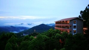 Um edifício com várias andares e varandas, cercado por vegetação exuberante e montanhas ao fundo.
