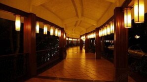 Um corredor com chão de azulejos e colunas de madeira, iluminado por luminárias pendentes.
