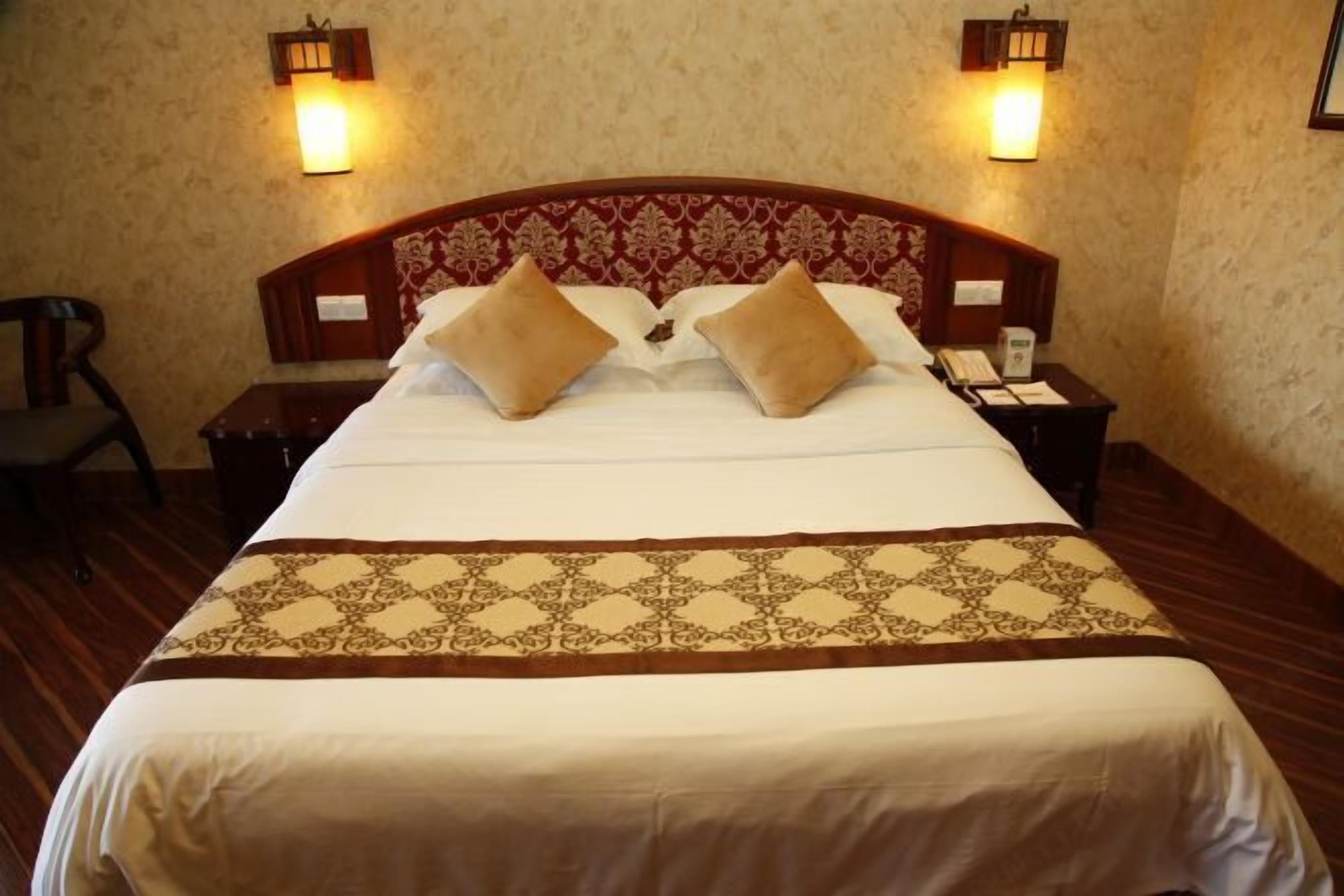 A neatly made bed with a patterned bedspread, two bedside lamps, and a wooden headboard.