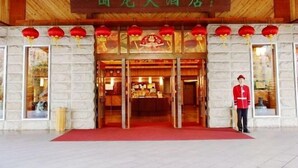 Entrada de um hotel em estilo tradicional chinês, com uma placa, lanternas vermelhas e um atendente uniformizado.