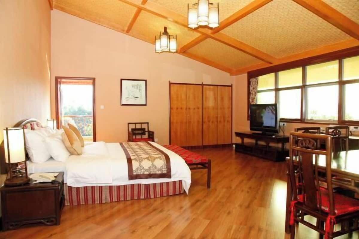 A bedroom with a bed, wooden flooring, a television, and a large window.