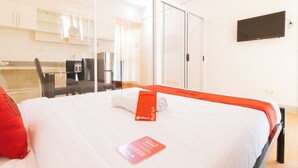 A hotel room with a bed, a desk, a chair, a flat-screen TV, and a kitchen area. - Reddoorz Plus @ Alpina Heights Paranaque (Parañaque)