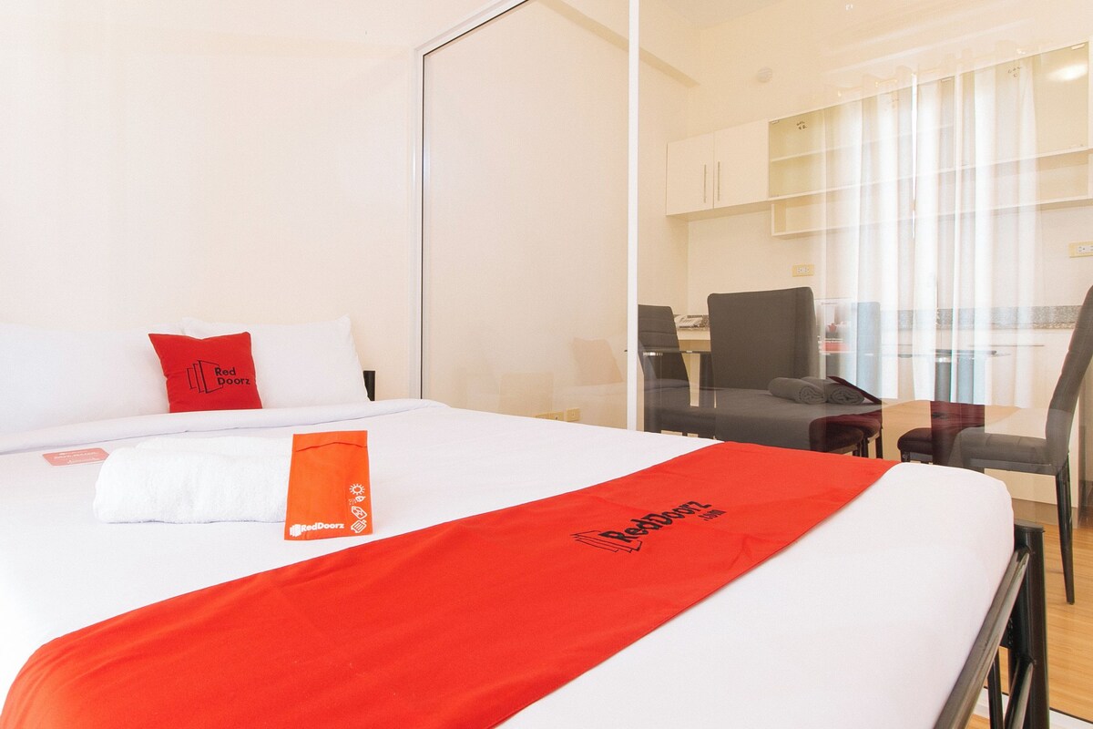 A hotel room with a bed, a red and white blanket, a red pillow, and a glass partition.