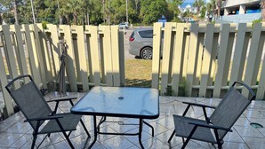 Pihalla on patio, jossa on pöytä ja kaksi tuolia, puisesta aita ja taustalla pysäköity auto.