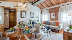 Uma sala de estar moderna com área de jantar, apresentando paredes de tijolo aparente, vigas de madeira e móveis contemporâneos.