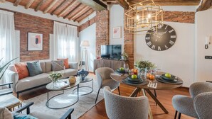 Uma sala de estar moderna com parede de tijolos, um relógio grande, um sofá e uma mesa de jantar com frutas e copos.