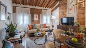 A cozy living room with a brick wall, a sofa, a coffee table, and a TV. - La Dorina Penthouse in Lucca (Lucca)