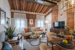 A cozy living room with a brick wall, a sofa, a coffee table, and a TV. - La Dorina Penthouse in Lucca (Lucca)