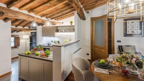 Cozinha com ilha central, vigas de madeira no teto, luminárias pendentes e área de jantar com mesa posta para dois.