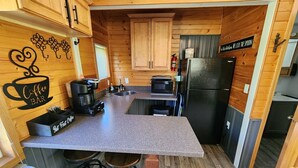 A compact kitchen with wooden cabinets, a coffee station, a microwave, and a refrigerator. - Studio Cottage at Lake Road Campground, on the beautiful Mississippi River. (Trempealeau)