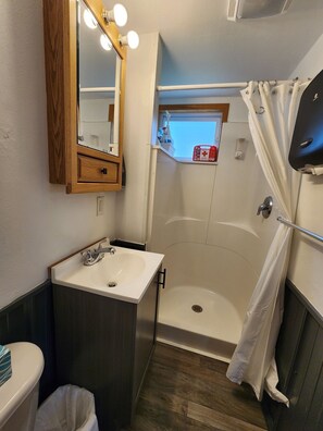 Een badkamer met een houten wastafelmeubel, een wastafel, een spiegel, een douche en een raam boven de douche.