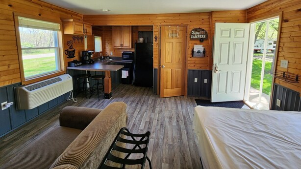 A compact cabin with a kitchenette, a dining area, and a bedroom. - Studio Cottage at Lake Road Campground, on the beautiful Mississippi River. (Trempealeau)