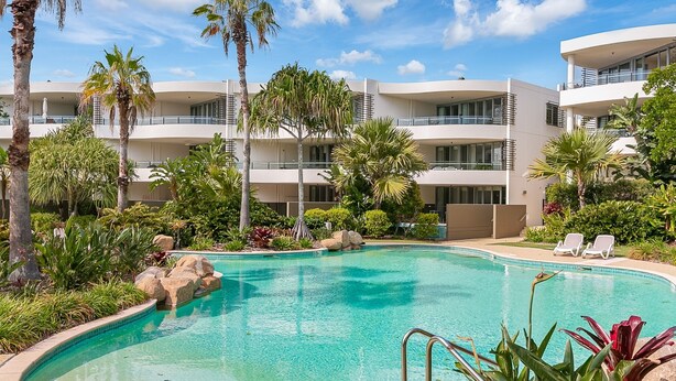A resort pool surrounded by palm trees and a multi-story building with balconies. - Boasting coveted north facing views and an unrivalled coastal lifestyle. (Tweed)