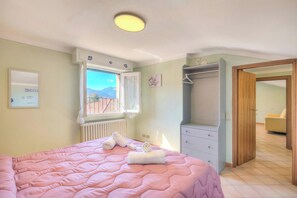 Une chambre à coucher avec un lit, une fenêtre donnant sur un paysage agréable, une armoire et une porte menant à une autre pièce.