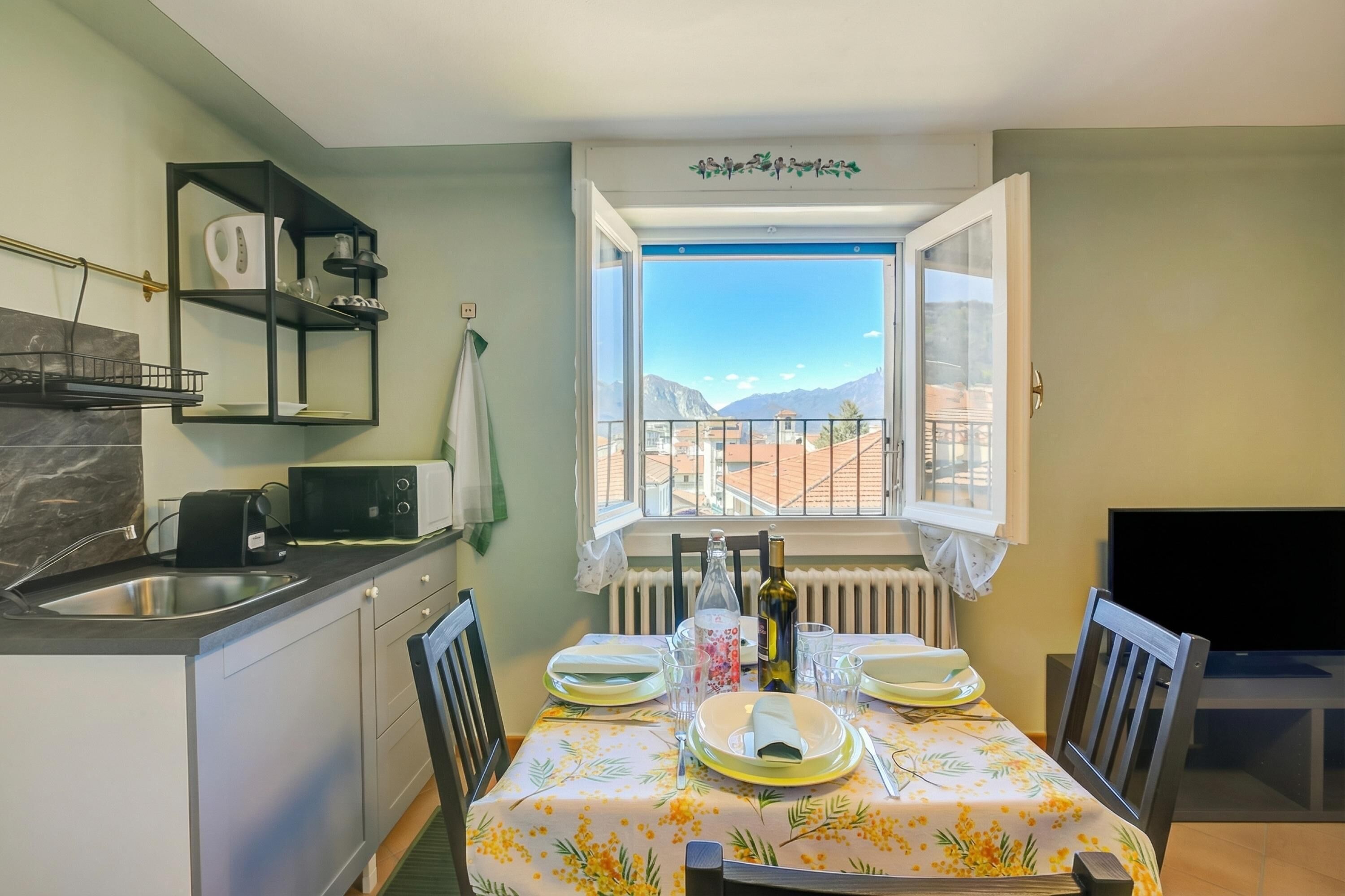 Ein Essbereich mit Tisch für vier Personen, eine Küche mit Mikrowelle und Blick auf Berge durch ein Fenster.
