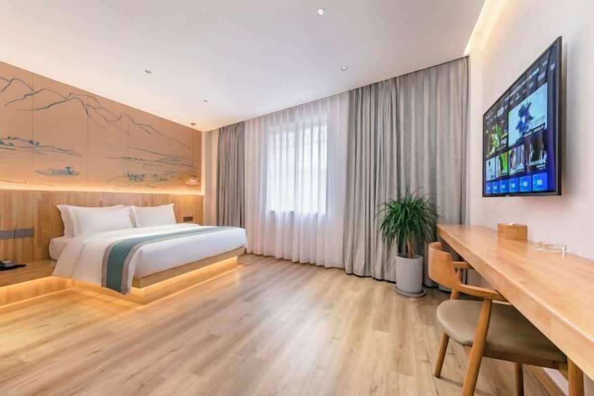 A modern hotel room with a bed, a desk, a large window with curtains, and a wall-mounted TV.