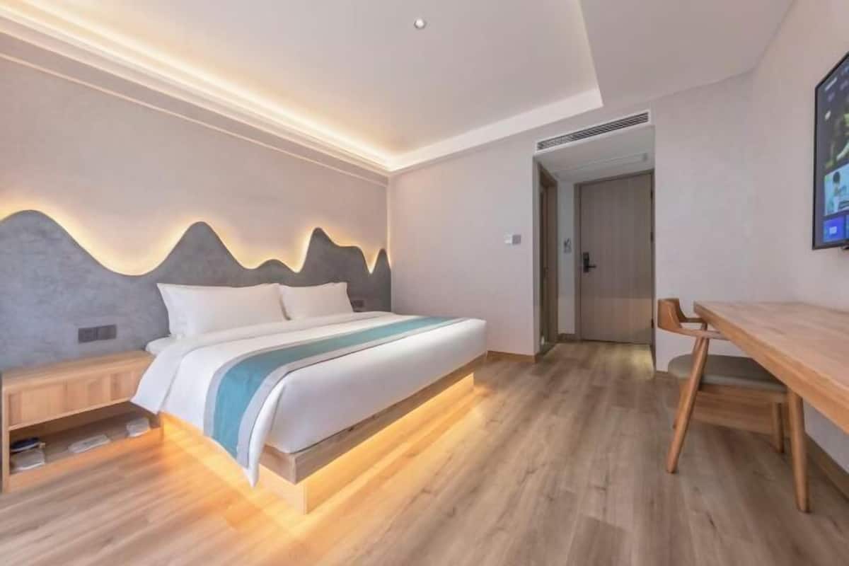 A modern bedroom with a bed, bedside tables, a wooden desk, and a wall-mounted TV.