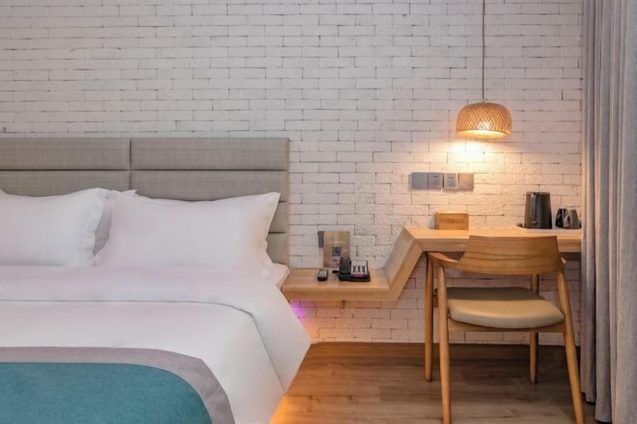 Habitación de hotel con cama, escritorio y silla. Hay una lámpara en el escritorio y una mesita con un hervidor y una taza.