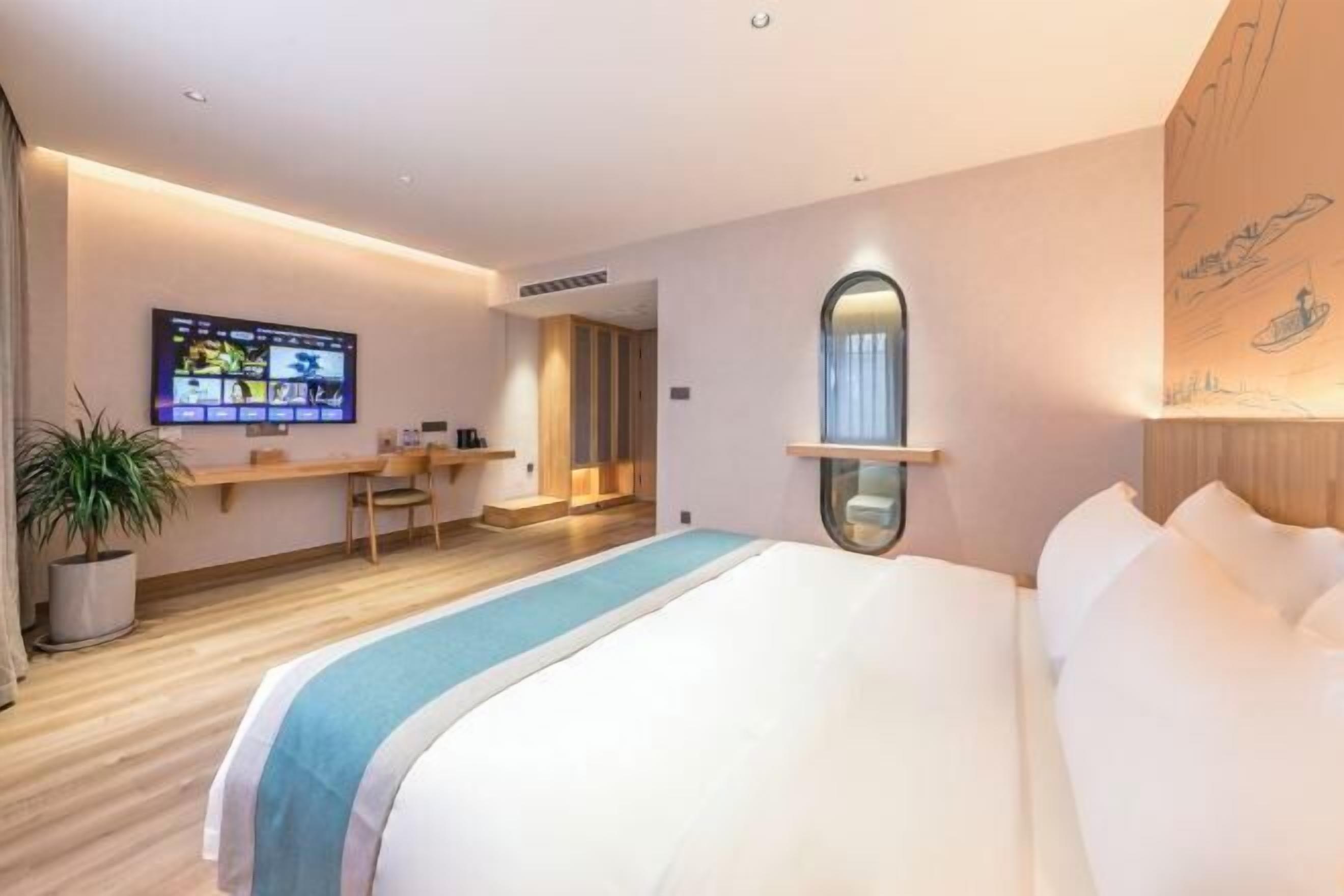 Ein Hotelzimmer mit Bett, Schreibtisch, Fernseher und Blumentopf.