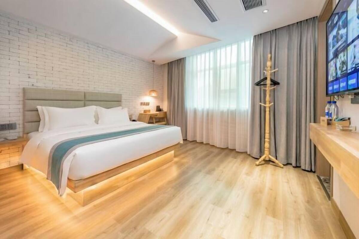 A modern hotel room with a bed, a wooden floor, a brick wall, a TV, and a lamp.