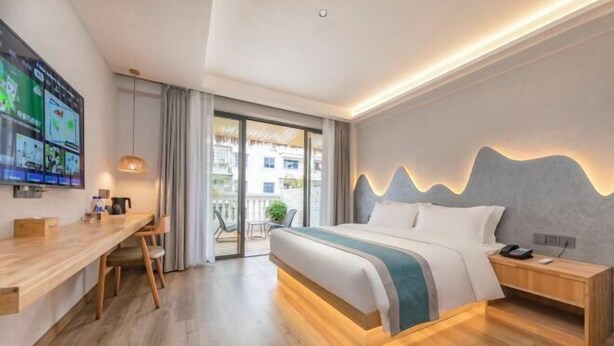 Una habitación de hotel moderna con un escritorio de madera, una cama con detalles azules, una mesita de noche y un televisor montado en la pared.