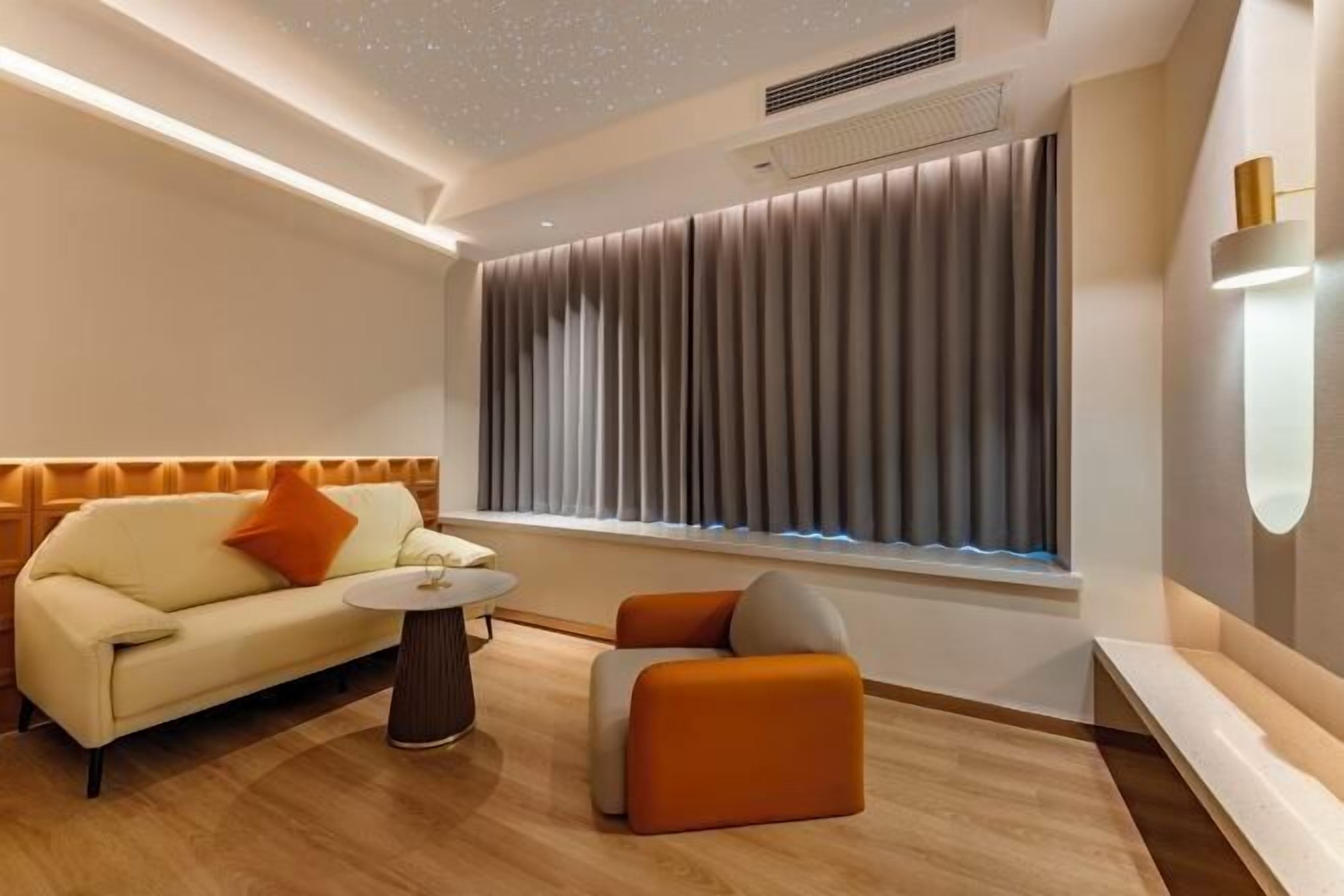 A modern hotel room with a sofa, ottoman, and a small table.