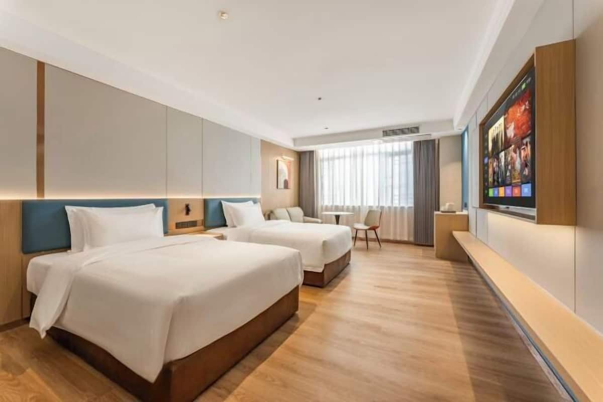 A hotel room with two beds, a TV mounted on the wall, and a seating area with a table and chairs.
