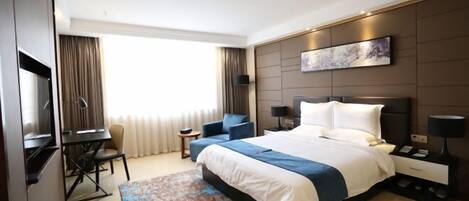 A modern hotel room with a large bed, a desk, a chair, and a television.