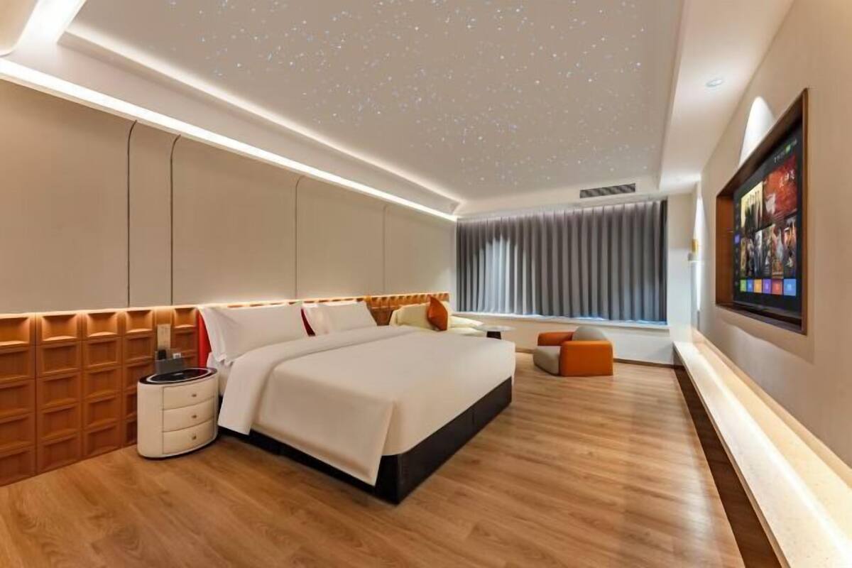 A modern hotel room with a large bed, a bedside table, a wall-mounted TV, and a ceiling with a starry design.