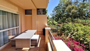 A balcony with a dining table and chairs, a sliding glass door, and a view of greenery and flowers. - SR Dunas de Carib Playa Marbella (Marbella)