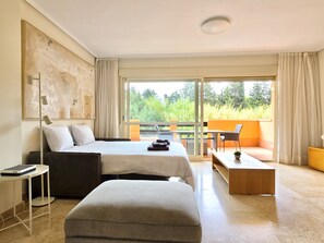 A modern hotel room with a bed, a desk, a chair, and a balcony with a view of greenery. - SR Dunas de Carib Playa Marbella (Marbella)