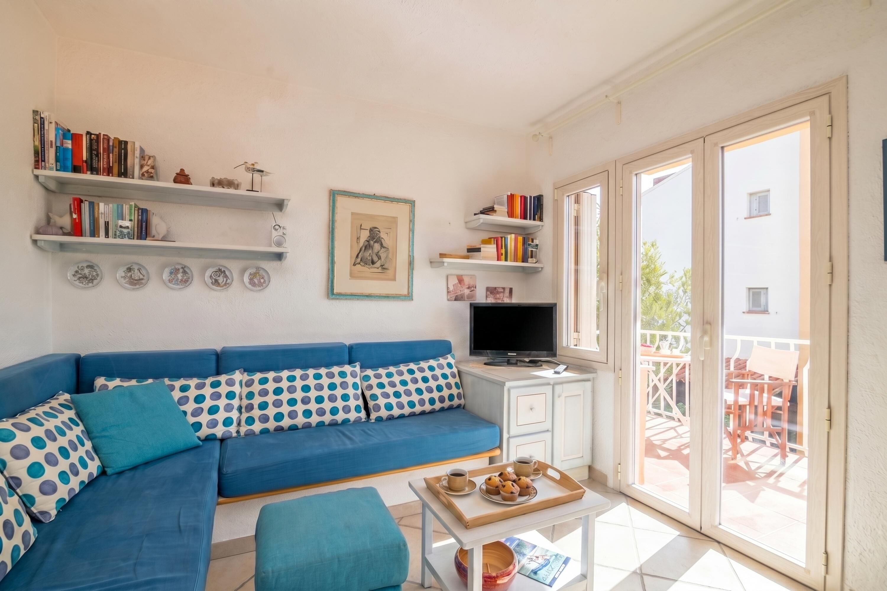 Una sala de estar con sofá azul, una mesa de centro, televisor y un balcón con mesa y sillas.