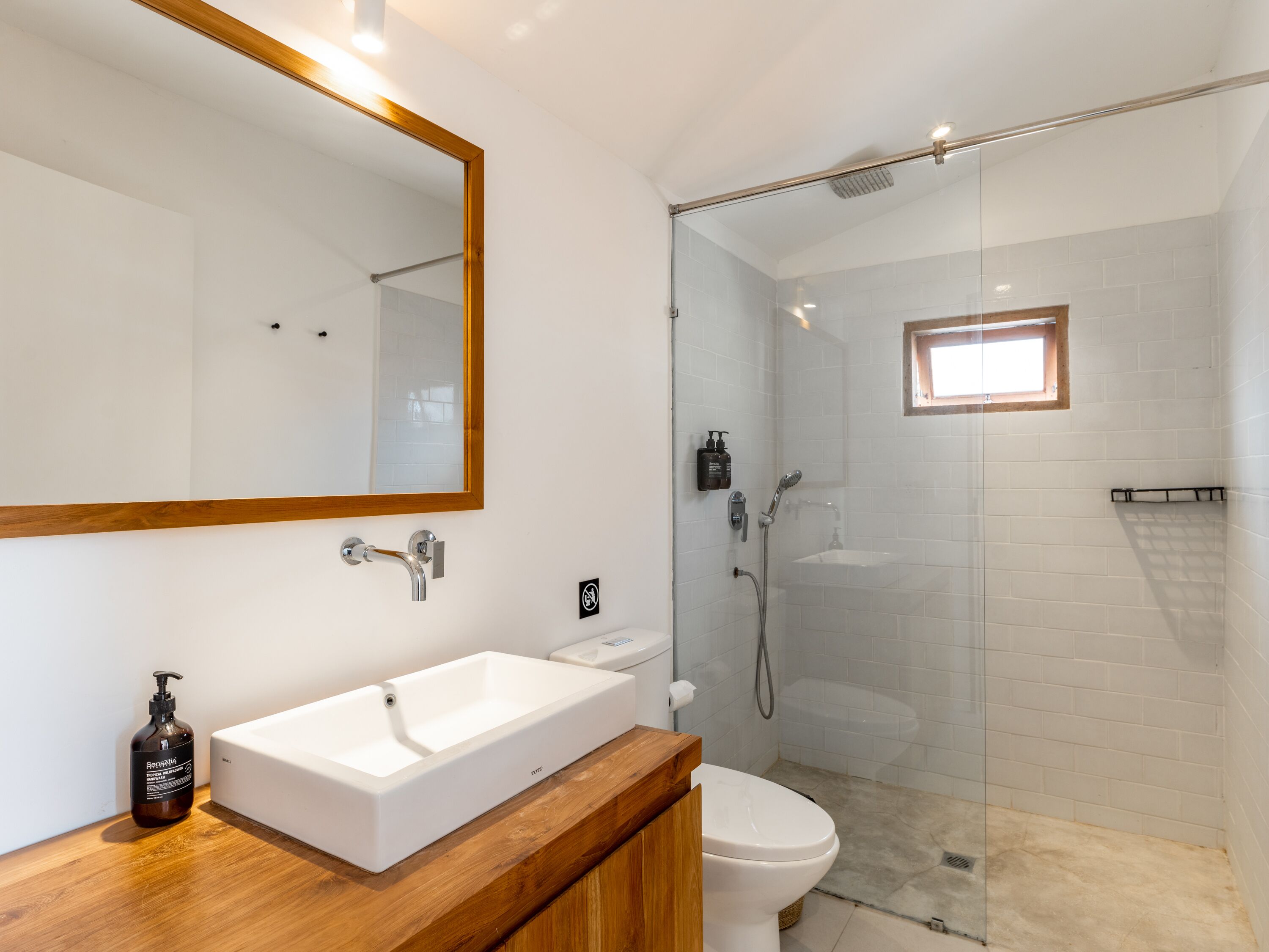 Une salle de bain avec un lavabo blanc, des toilettes, une douche avec une porte en verre et un miroir avec un cadre en bois.