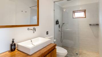 Une salle de bain avec un lavabo blanc, des toilettes, une douche avec une porte en verre et un miroir avec un cadre en bois.
