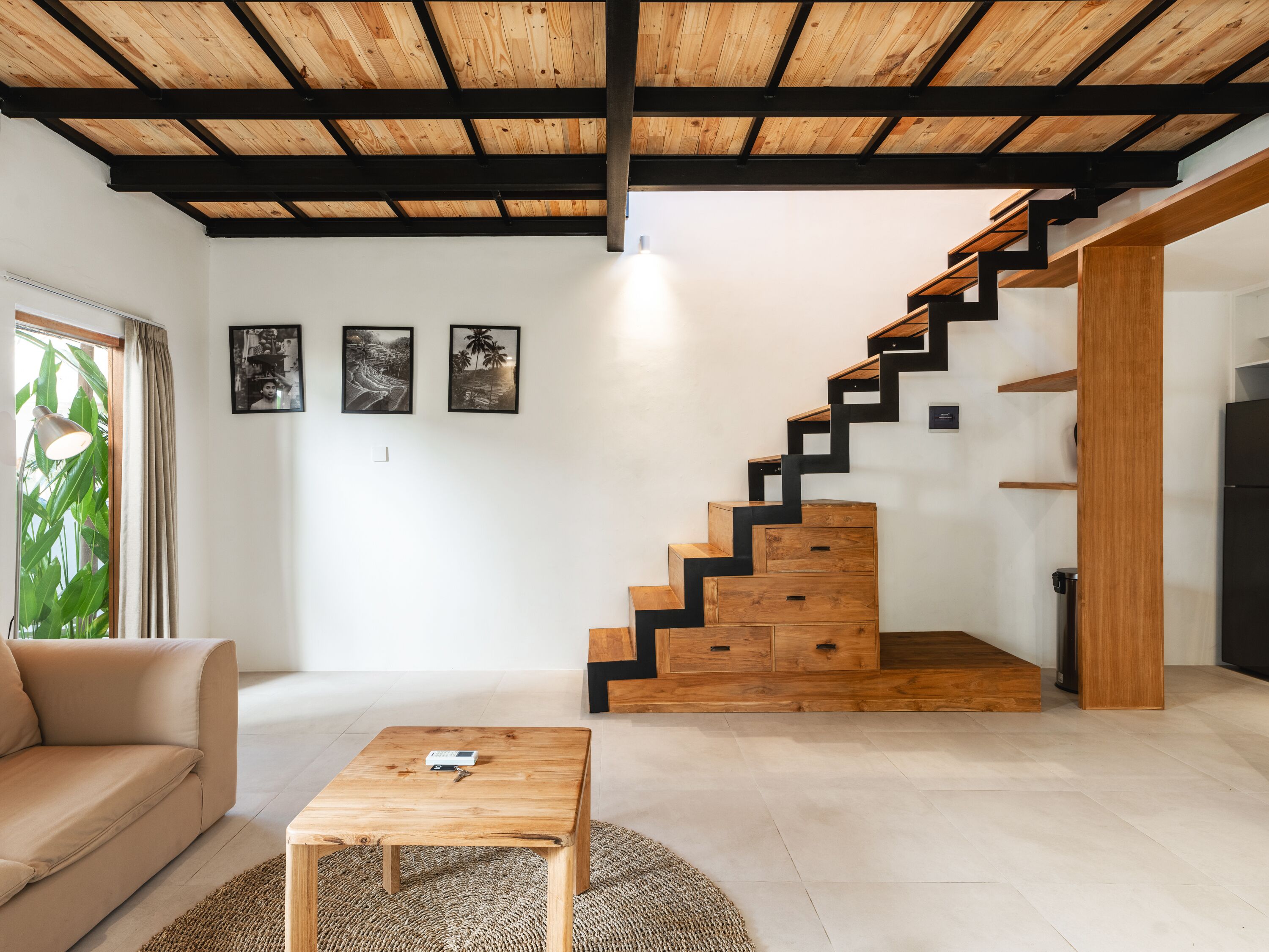 A modern living room with a wooden staircase, a sofa, a coffee table, and framed pictures on the wall.