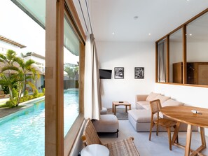 Una sala de estar moderna con vista a la piscina, un sofá, una mesa de comedor y un televisor en la pared.