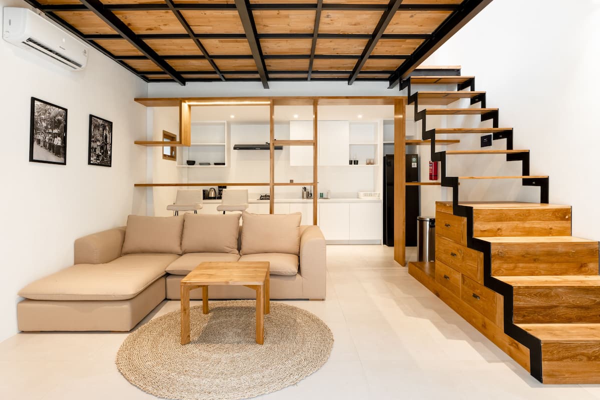 A modern living room with a sofa, a coffee table, and a staircase with wooden steps and black railings.