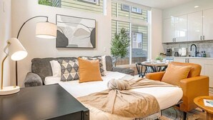 Una camera d'albergo moderna con un letto, una scrivania, una sedia, una lampada, un quadro e vista sulla cucina e all'esterno.