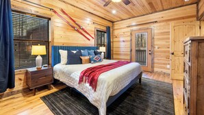 A wooden-paneled bedroom with a bed, nightstands, a ceiling fan, and a window with blinds.