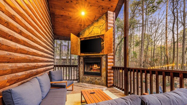 A log cabin with a stone fireplace, wooden deck, and outdoor seating area.